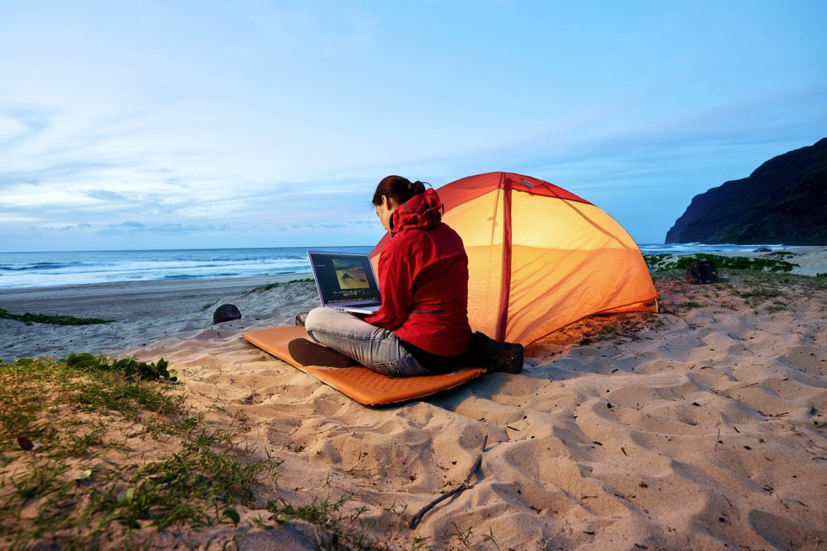 woman using laptop at tent on the beach at dusk